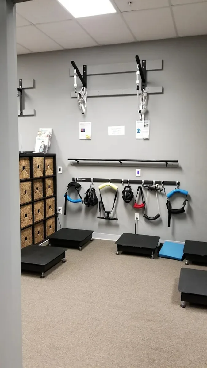 A rehabilitation room wall with a harness rig, resistance bands, step platforms and storage cubbies.