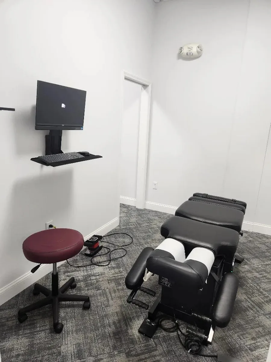A ChiroMed treatment room with a drop-piece adjustment table, a rolling stool and a wall-mounted monitor.