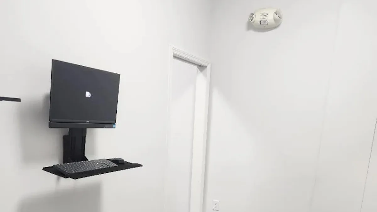 A ChiroMed treatment room with a drop-piece adjustment table, a rolling stool and a wall-mounted monitor.