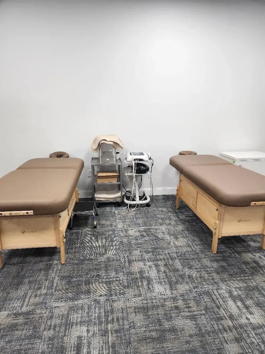 A treatment room set up with two padded tables and a therapy cart.